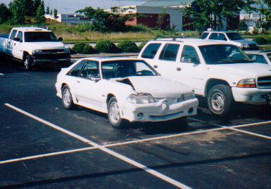 1982 Ford Bronco - White coupe with front-end damage parked in a lot.
