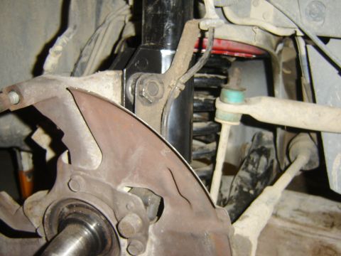 1987 Lincoln Mark VII - Detail view of a vehicle's front suspension system, showing the shock absorber, coil spring, and brake dust shield.