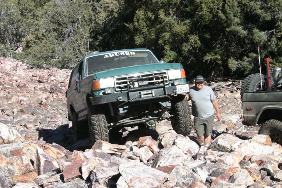 Green Ford Bronco with "ABUSED" sticker on windshield, navigating rocky terrain