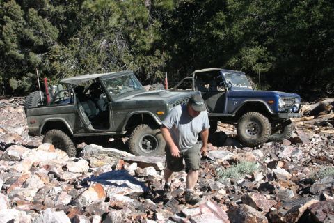 1991 Ford Bronco - Two classic Ford Broncos tackle a challenging off-road course in a wooded, rocky environment.