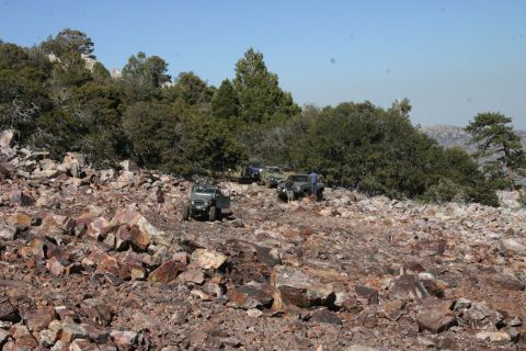 1991 Ford Bronco - Several off-road vehicles traverse a challenging, rocky terrain on a sunny day.