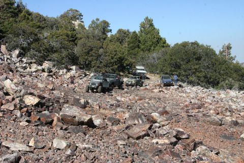 1991 Ford Bronco - Multiple 4x4 vehicles traverse a challenging rocky mountain path under a bright blue sky.