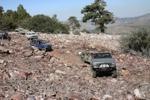 1991 Ford Bronco - Multiple off-road vehicles traverse a challenging rocky trail under a clear blue sky.