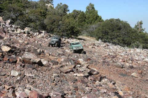 1991 Ford Bronco - Two off-road vehicles traverse a challenging, rocky terrain under a clear blue sky.