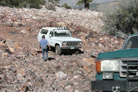 1991 Ford Bronco - A white Ford Bronco navigates a rocky off-road path, with another vehicle partially visible in the foreground.