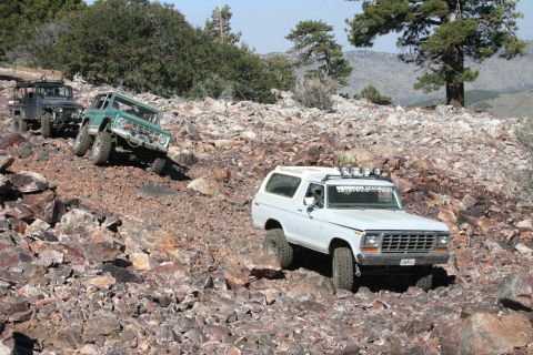 1991 Ford Bronco - Three off-road vehicles navigate a steep, rocky incline in a mountainous landscape.