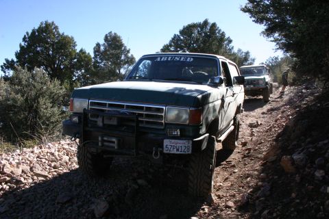 1991 Ford Bronco - Two off-road vehicles navigate a rocky trail under a clear blue sky.