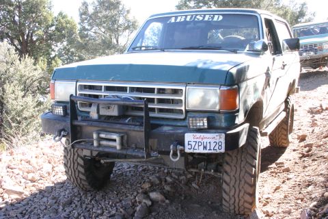 1991 Ford Bronco - A green Ford Bronco navigates a rocky off-road path, with another vehicle visible behind it.