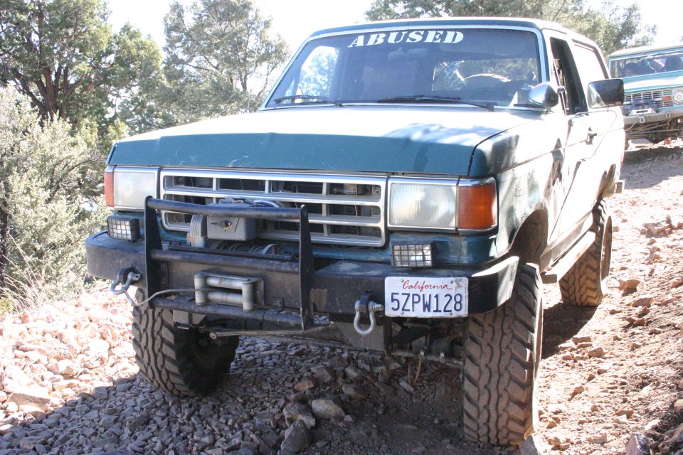 Green 1987 Ford Bronco with aftermarket bumper and winch, on a rocky trail