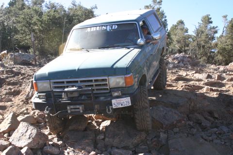 1991 Ford Bronco - Ford Bronco with 'ABUSED' sticker on windshield is shown off-roading over rocks.