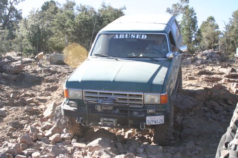 1991 Ford Bronco - This green Ford Bronco navigates a challenging rocky terrain, displaying the word "ABUSED" on its windshield.