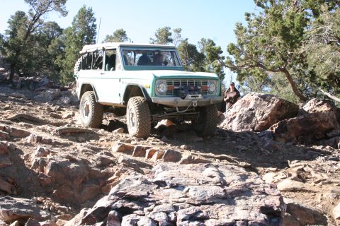 1991 Ford Bronco - A classic Ford Bronco navigates a challenging rocky trail under a clear blue sky.