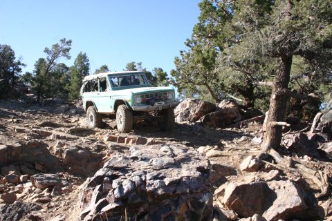 1991 Ford Bronco - A classic Ford Bronco tackles a challenging rocky terrain under a clear blue sky.