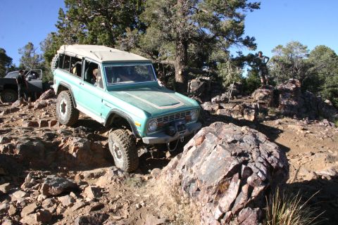 1991 Ford Bronco - A teal Ford Bronco navigates a challenging rocky terrain, with another vehicle visible in the background.