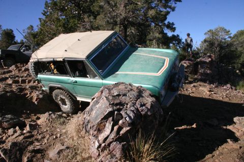 1991 Ford Bronco - A green SUV is shown off-roading on a rocky terrain with a person standing on a hill in the background.