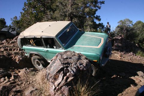 1991 Ford Bronco - A green Ford Bronco navigates a challenging rocky terrain with a person standing on a ridge in the background.