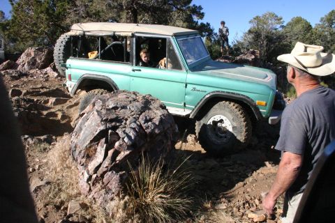 1991 Ford Bronco - A green Ford Bronco tackles a challenging rocky terrain, with a person watching from the side.