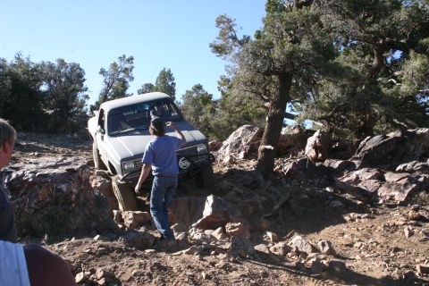 1991 Ford Bronco - A gray pickup truck is shown off-roading on a rocky trail under a clear blue sky.