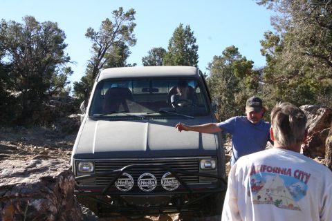 1991 Ford Bronco - A man gestures towards a gray pickup truck navigating a rocky off-road trail.