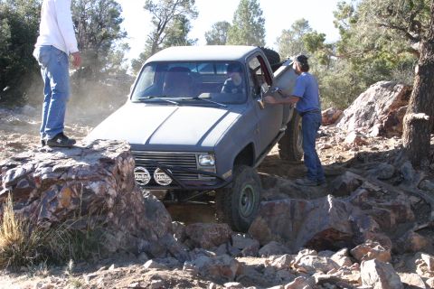 1991 Ford Bronco - A gray pickup truck maneuvers through a challenging rocky off-road course with two people observing.