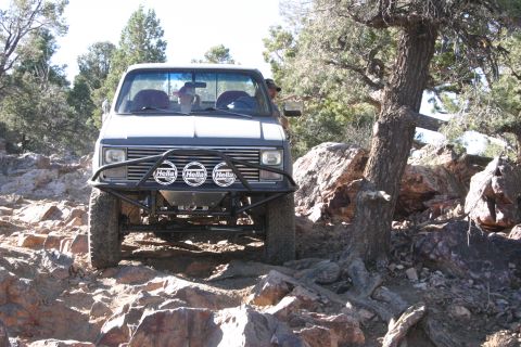 1991 Ford Bronco - Off-road pickup truck navigating rocky terrain with a custom bumper and auxiliary lights.
