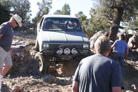 1991 Ford Bronco - A gray pickup truck, likely from the 1980s, is shown tackling a challenging off-road course with several people observing.
