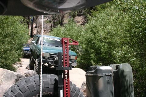1991 Ford Bronco - Two off-road vehicles navigate a challenging rocky path surrounded by dense foliage.
