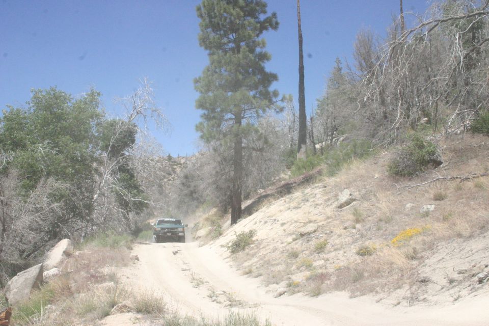 Green SUV drives up a dusty dirt road through a dry, wooded area