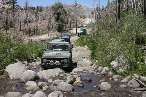 1991 Ford Bronco - A group of off-road vehicles navigates a challenging, rocky path in a dry, wooded landscape.