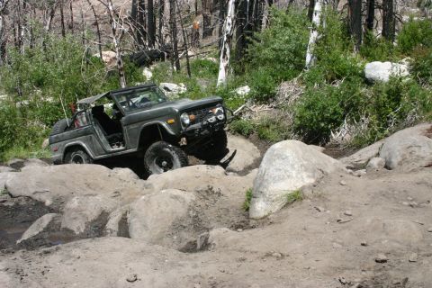 1991 Ford Bronco - A dark green Ford Bronco tackles a challenging rocky trail with its top off.