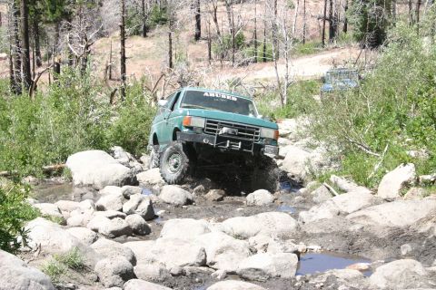 1991 Ford Bronco - Green 1991 Ford Bronco tackles a challenging off-road obstacle course with a second vehicle in the distance.