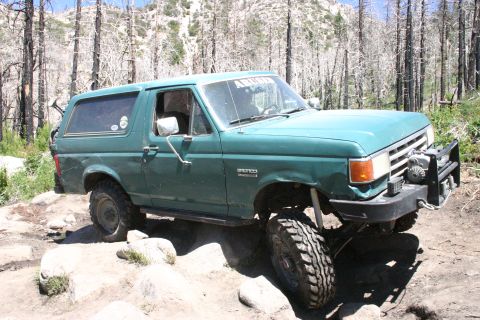 1991 Ford Bronco - A green Ford Bronco navigates a rocky trail in a wooded area.