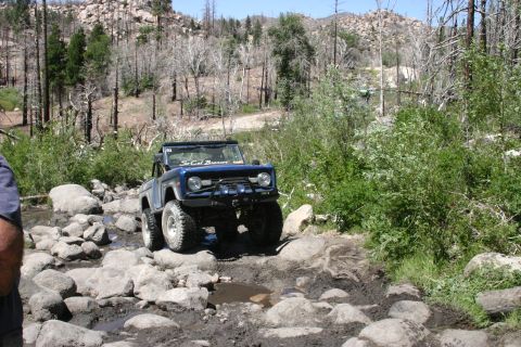 1991 Ford Bronco - This blue Ford Bronco is shown off-roading on a challenging rocky and muddy path.