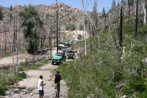 1991 Ford Bronco - A group of off-road vehicles navigates a rocky trail in a wooded area with evidence of a past fire.