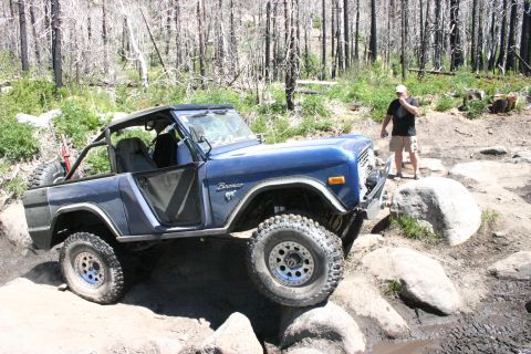 1991 Ford Bronco - Blue Ford Bronco tackles rocky terrain on an off-road trail.