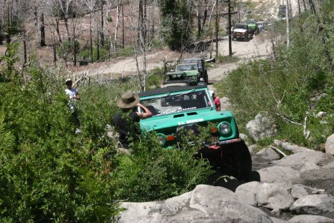 1991 Ford Bronco - A line of off-road vehicles, including a green Ford Bronco, traverse a challenging rocky path.