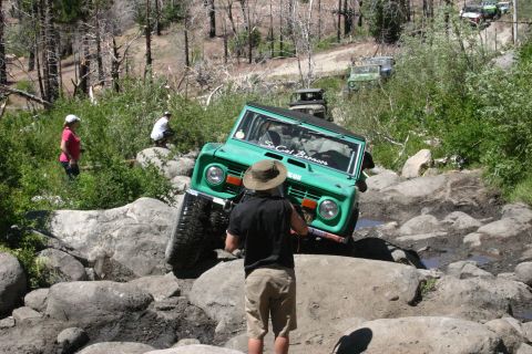 1991 Ford Bronco - A green Ford Bronco tackles a challenging rocky trail, with other vehicles visible in the background.