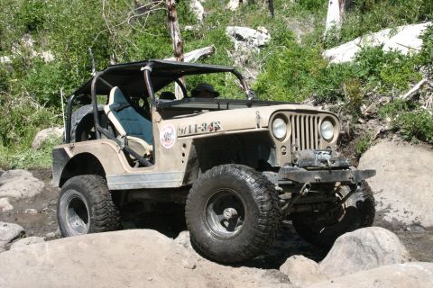 1991 Ford Bronco - A tan Jeep CJ-7 navigates a rocky trail, equipped for off-road adventure.