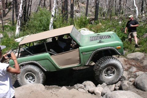 1991 Ford Bronco - This classic Ford Bronco is tackling a challenging off-road trail with large rocks and trees surrounding it.