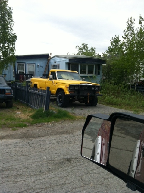 1986 Ford F-150 - A yellow Jeep J-10 pickup truck is parked in a driveway next to a fence and a mobile home.