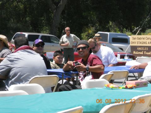 1986 Ford Bronco - A group of people are seated at tables outdoors, with several vehicles visible in the background.