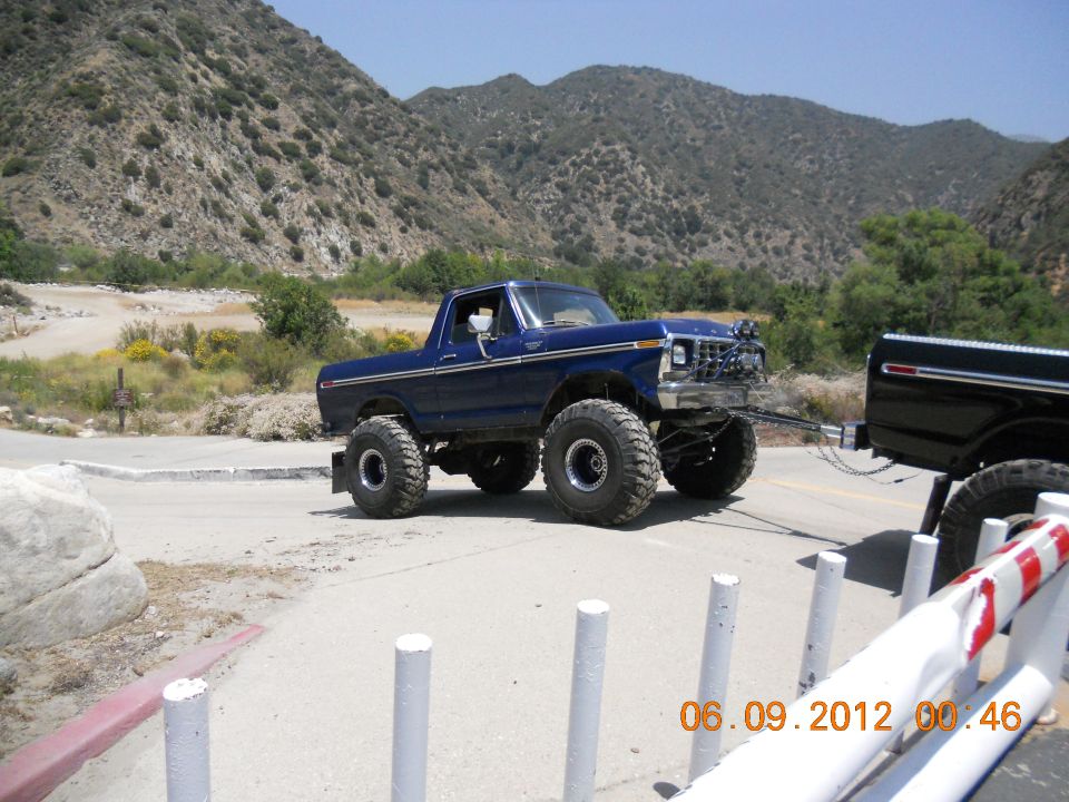 Blue lifted pickup truck towing a black pickup truck on a road with mountains in the background