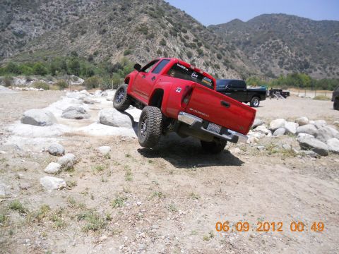1986 Ford Bronco - A red pickup truck navigates a rocky obstacle course with another truck in the background.
