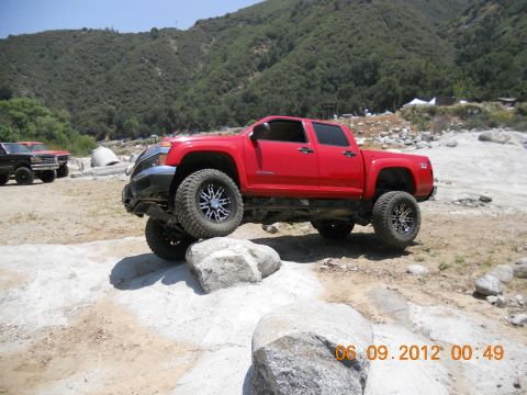 1986 Ford Bronco - A red pickup truck is shown off-roading on a rocky path with a second vehicle in the background.