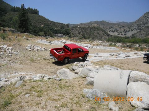 1986 Ford Bronco - A red pickup truck navigates a rocky, off-road course under a clear blue sky.