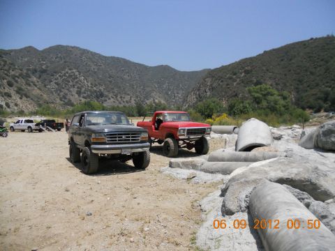 1986 Ford Bronco - Two modified trucks are parked in a rocky, mountainous area on a sunny day.