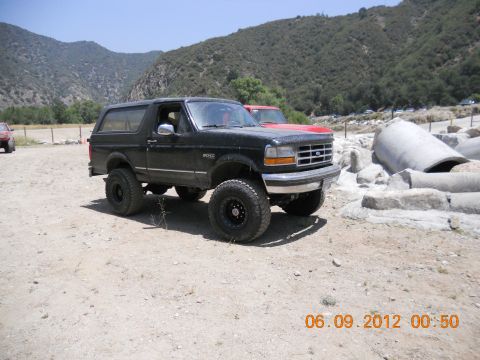 1986 Ford Bronco - A black Ford Bronco SUV is parked in a rocky, outdoor area with mountains in the background.