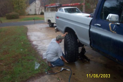 1979 Ford F-150 - Changing a tire on a 1979 Ford F-150, with a utility truck in the background.
