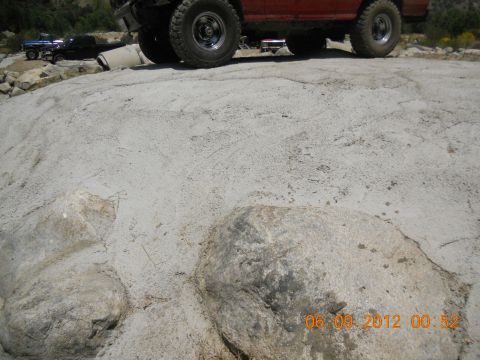 1986 Ford Bronco - Two off-road vehicles navigate a rocky, uneven landscape under a bright sky.