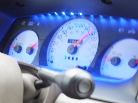 2003 Ford Crown Victoria - Motion-blurred white gauge cluster under blue backlight showing speed and gear selector.